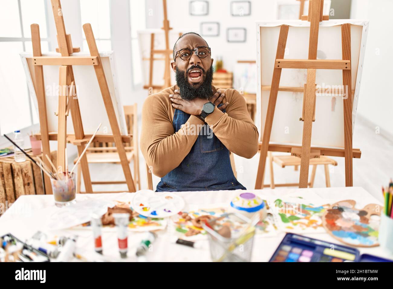 Artiste afro-américain homme au studio d'art criant et suffoquer parce que la douleur de strangle. Problème de santé. Asphyxiate et suicide concept. Banque D'Images