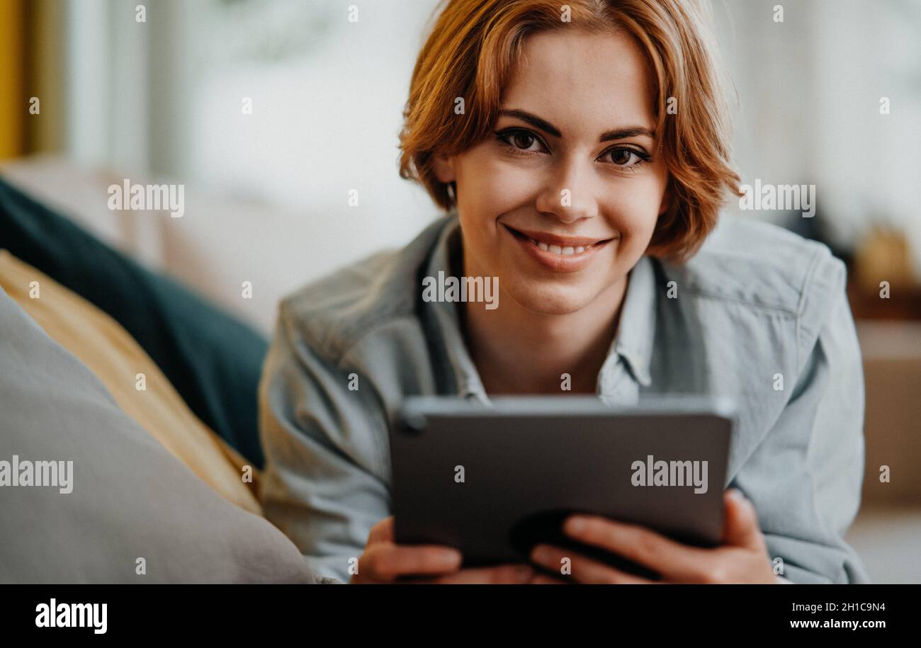 Portrait d'une jeune femme heureuse utilisant une tablette, allongé sur un canapé à la maison, regardant l'appareil photo Banque D'Images