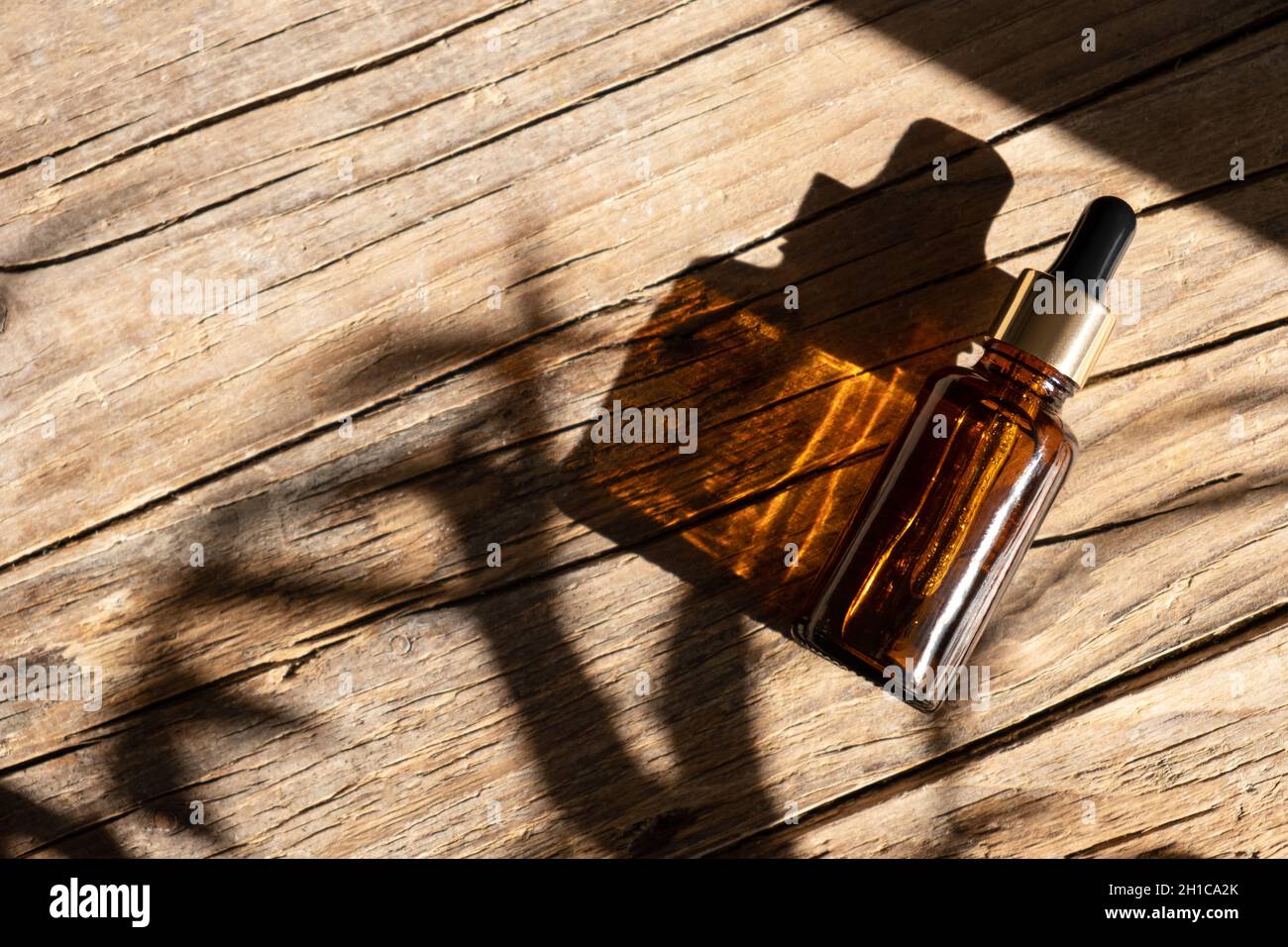 Bouteille en verre ambré foncé pour l'huile, la lotion ou le sérum sur un fond en bois vieilli avec une ombre dure de feuilles de palmier tropicales.Présentation d'un produit cosmétique.Mise en page de la marque du salon de beauté. Banque D'Images