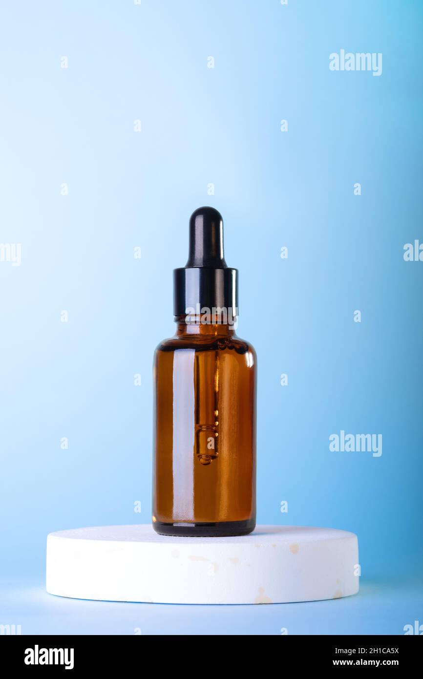 Flacons à cosmétiques compte-gouttes en verre ambré, podium blanc sur fond bleu pastel.Scène avec des formes géométriques.Vitrine. Banque D'Images