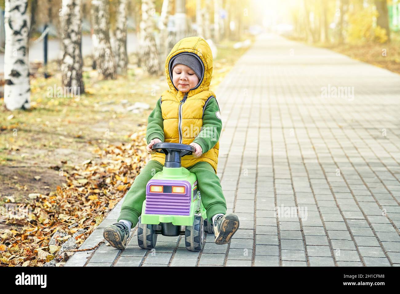 Joyeux petit garçon enfant dans un gilet jaune vif pousse le jouet tout en  marchant sur une route pavée dans un parc d'automne ensoleillé Photo Stock  - Alamy