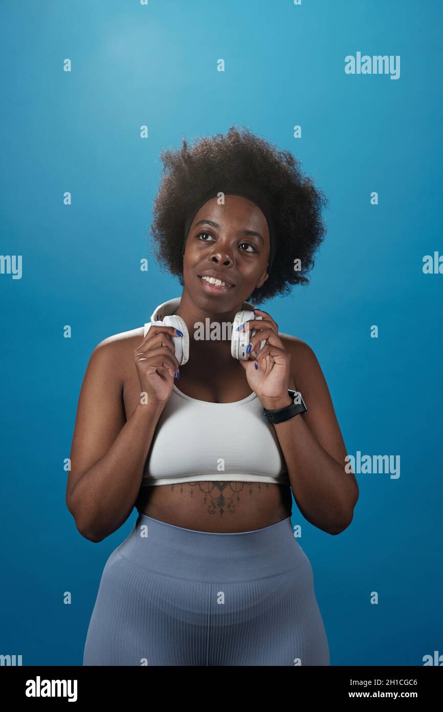 Jeune femme de taille plus en casque d'activité, en contact avec le casque tout en se tenant sur fond bleu Banque D'Images