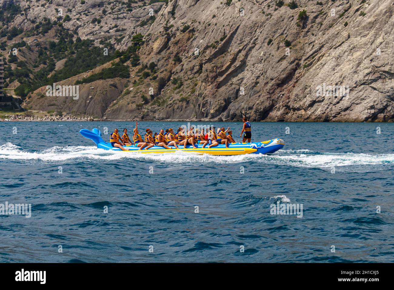 Une foule de personnes dans des gilets de sauvetage dans la mer sur une banane gonflable en caoutchouc contre une côte rocheuse.Une des activités de la station balnéaire.Republ Banque D'Images