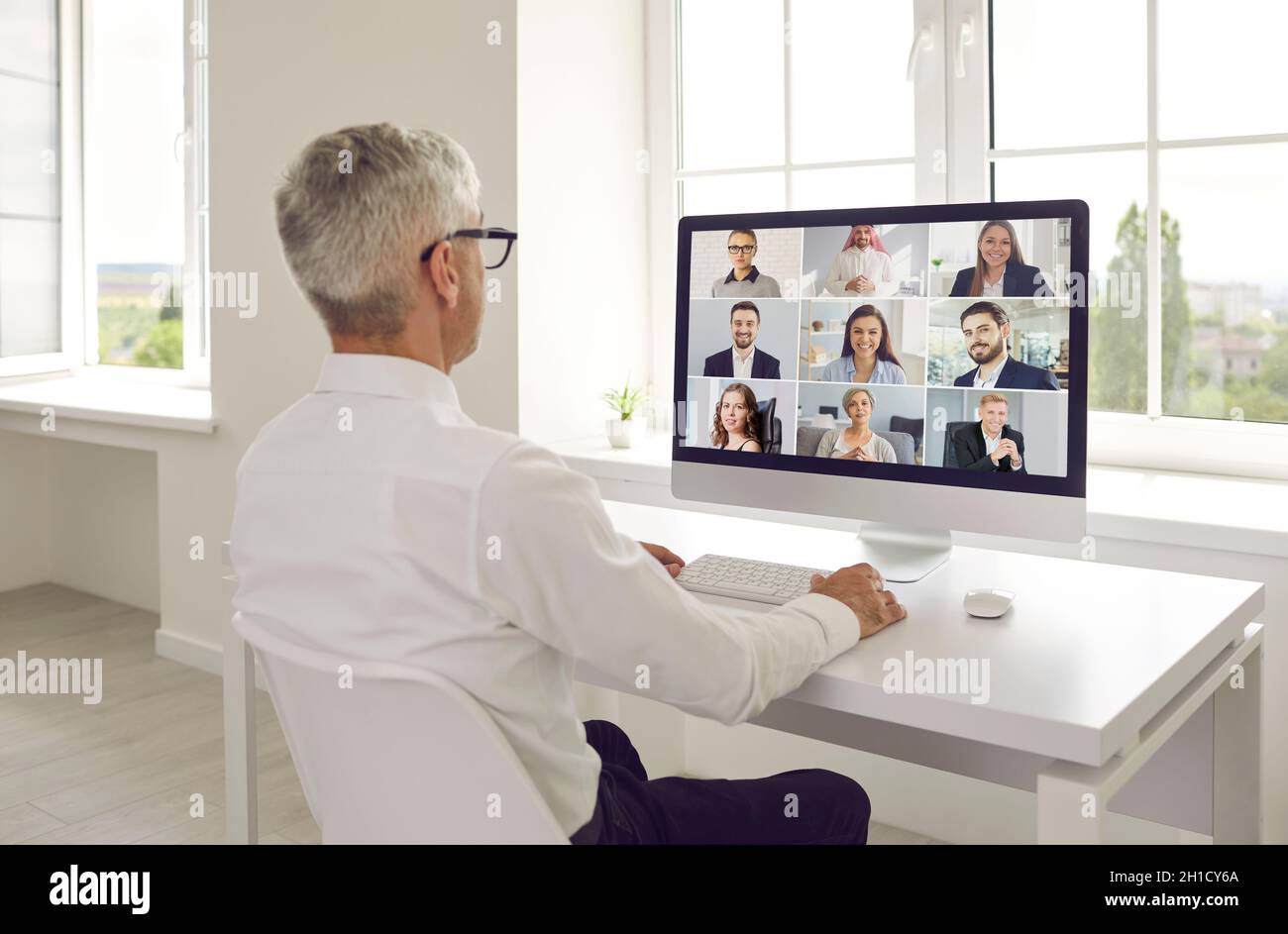 Homme assis à un bureau avec un ordinateur et tenant une réunion en ligne avec son équipe d'affaires Banque D'Images