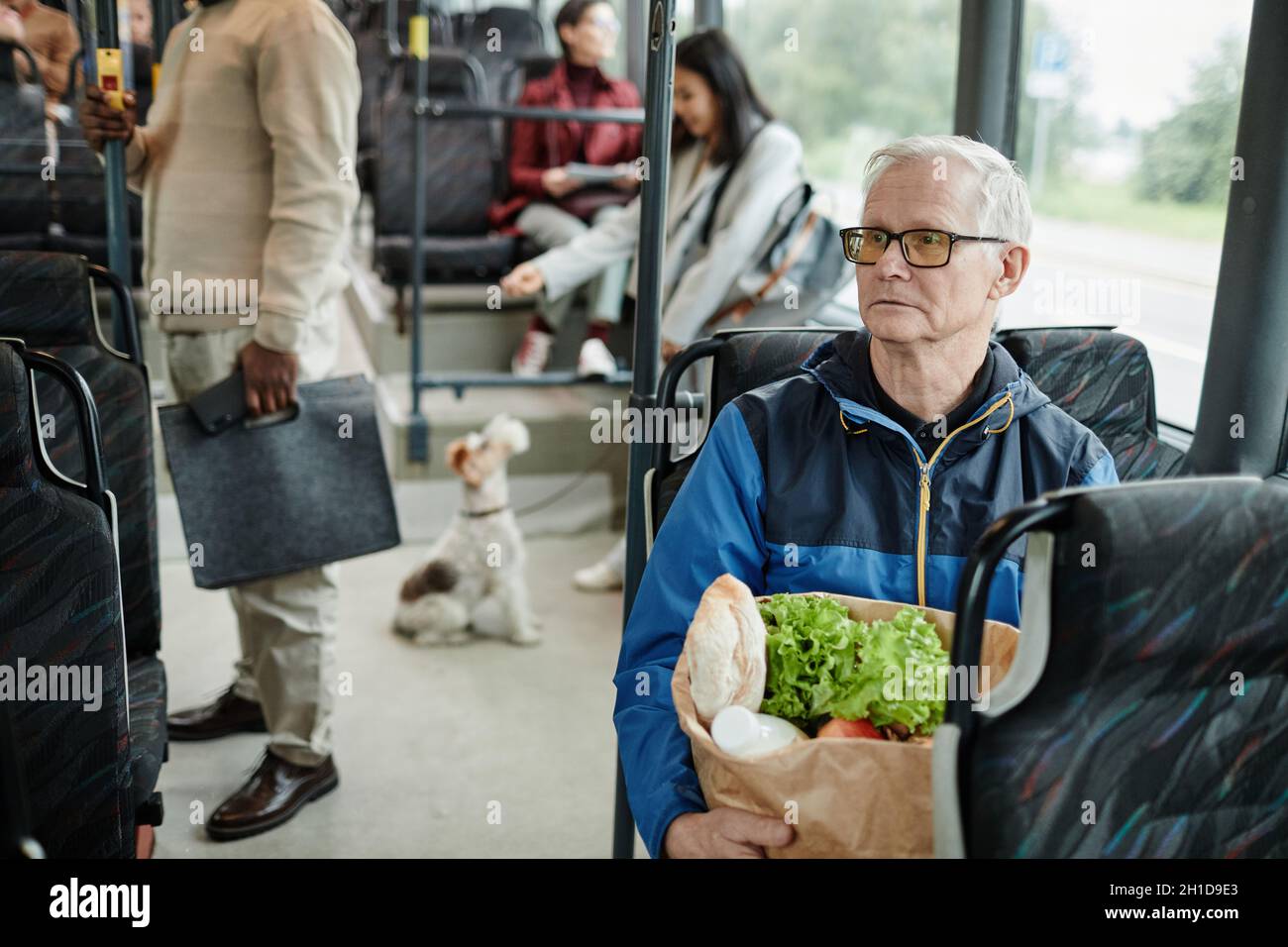 Portrait d'un homme âgé assis dans un bus lors d'un voyage en ville en transports en commun et tenant un sac en papier avec des provisions, un espace de photocopie Banque D'Images