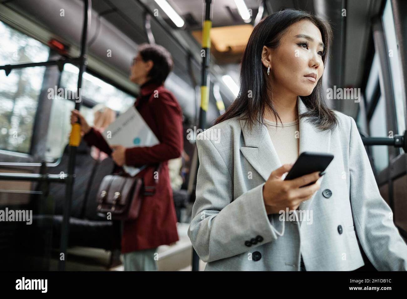 Portrait d'une élégante femme asiatique regardant la fenêtre dans le bus tout en voyageant en transports en commun et en tenant un smartphone, un espace de copie Banque D'Images