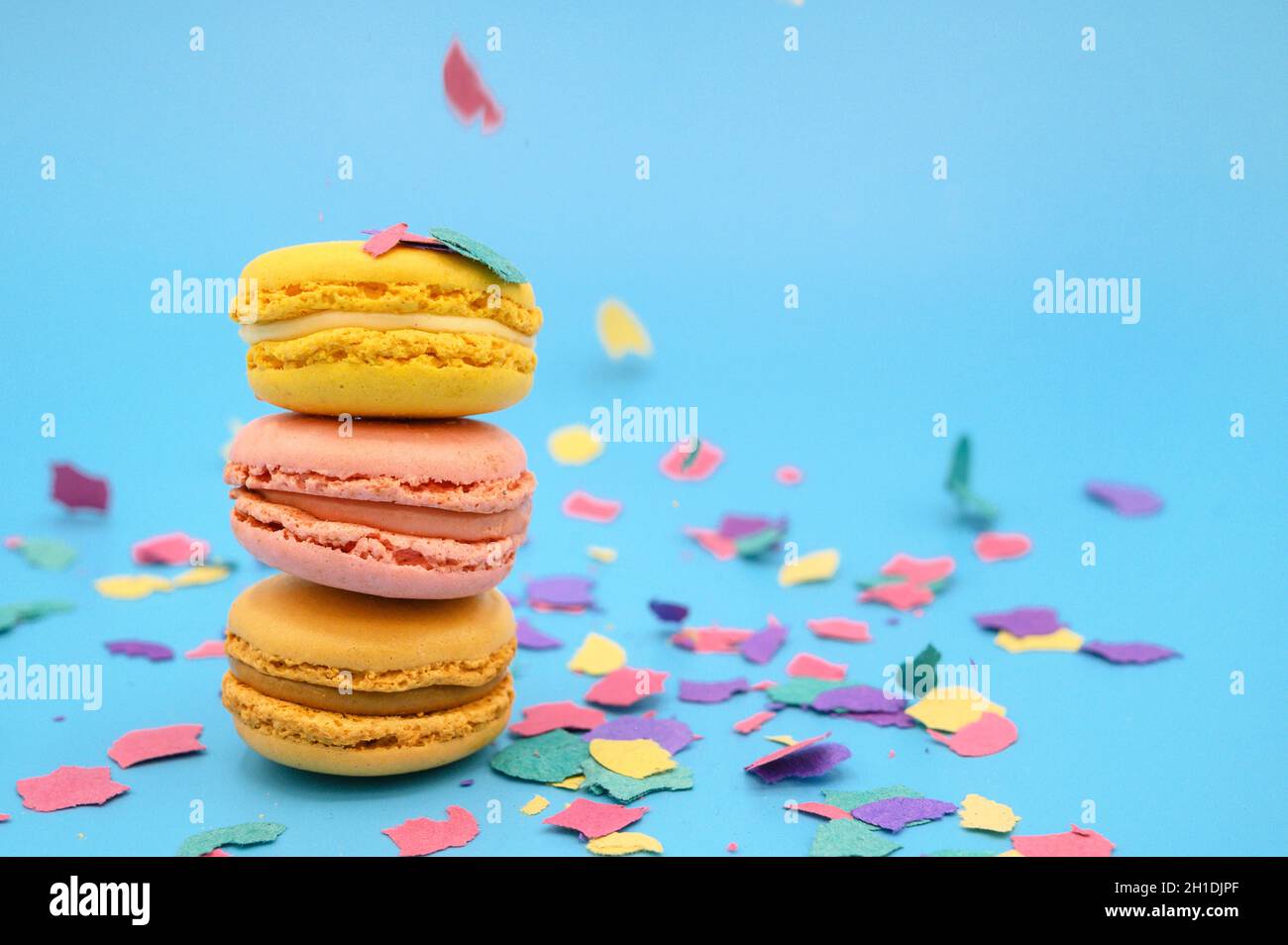 Macarons colorés sur papier bleu pastel tendance avec confettis. Macarons roses, jaunes et bruns savoureux. Banque D'Images