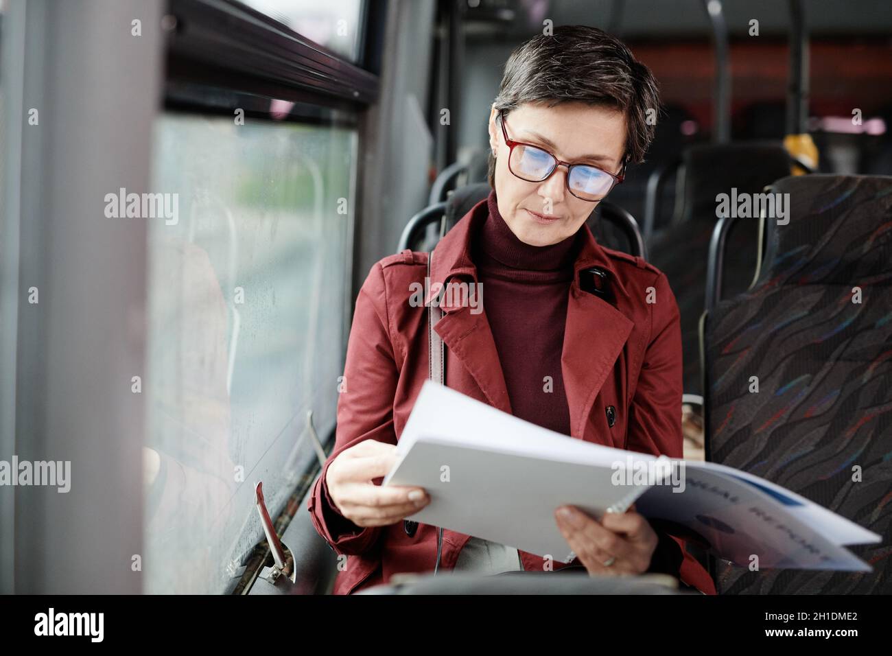 Portrait d'une élégante femme mûre lisant un livre en bus tout en voyageant en transports en commun dans la ville, espace copie Banque D'Images
