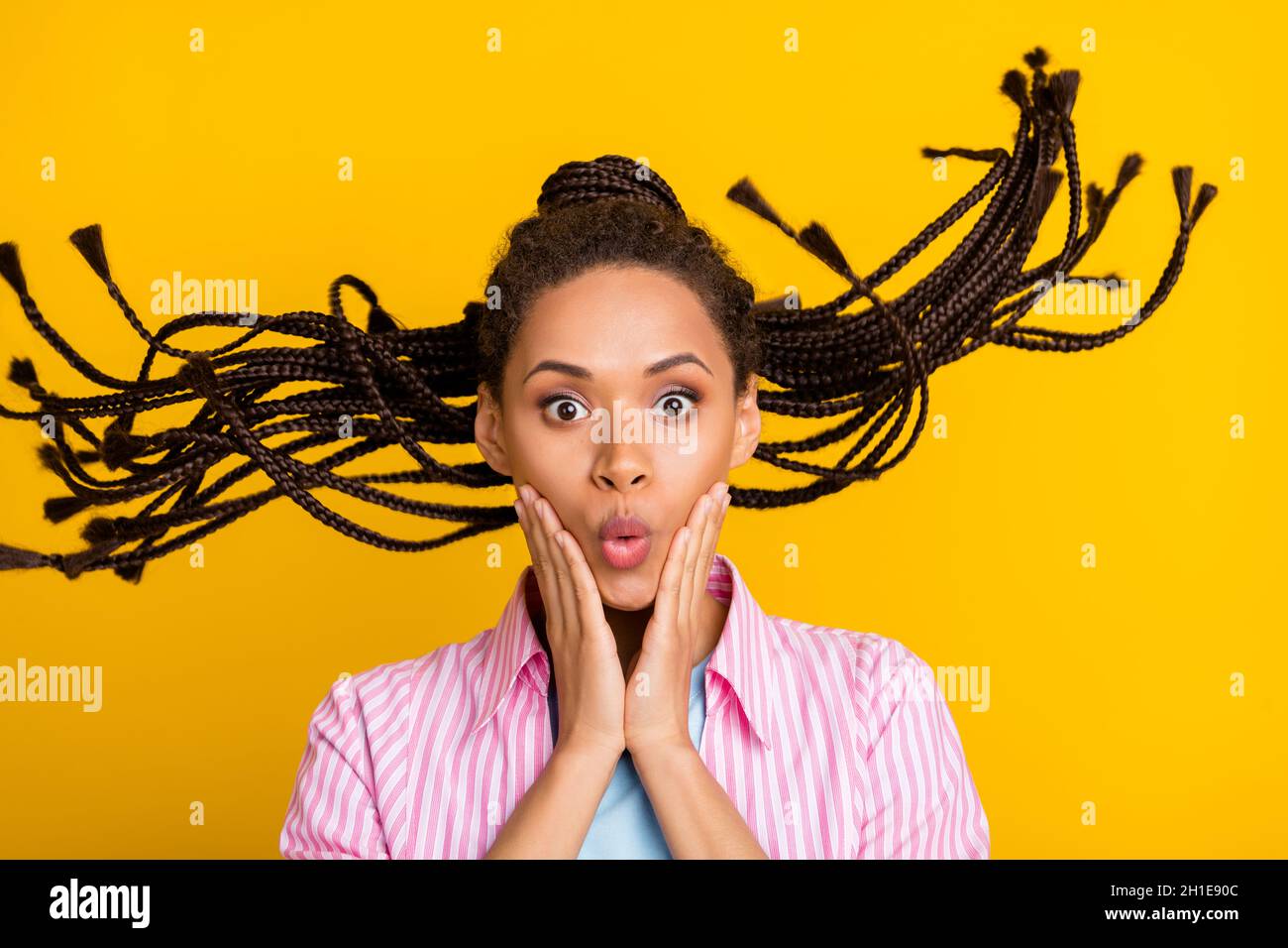 Photo de jeune afro-américain étonné choqué femme tenir les mains joues cheveux mouche isolée sur fond jaune de couleur Banque D'Images