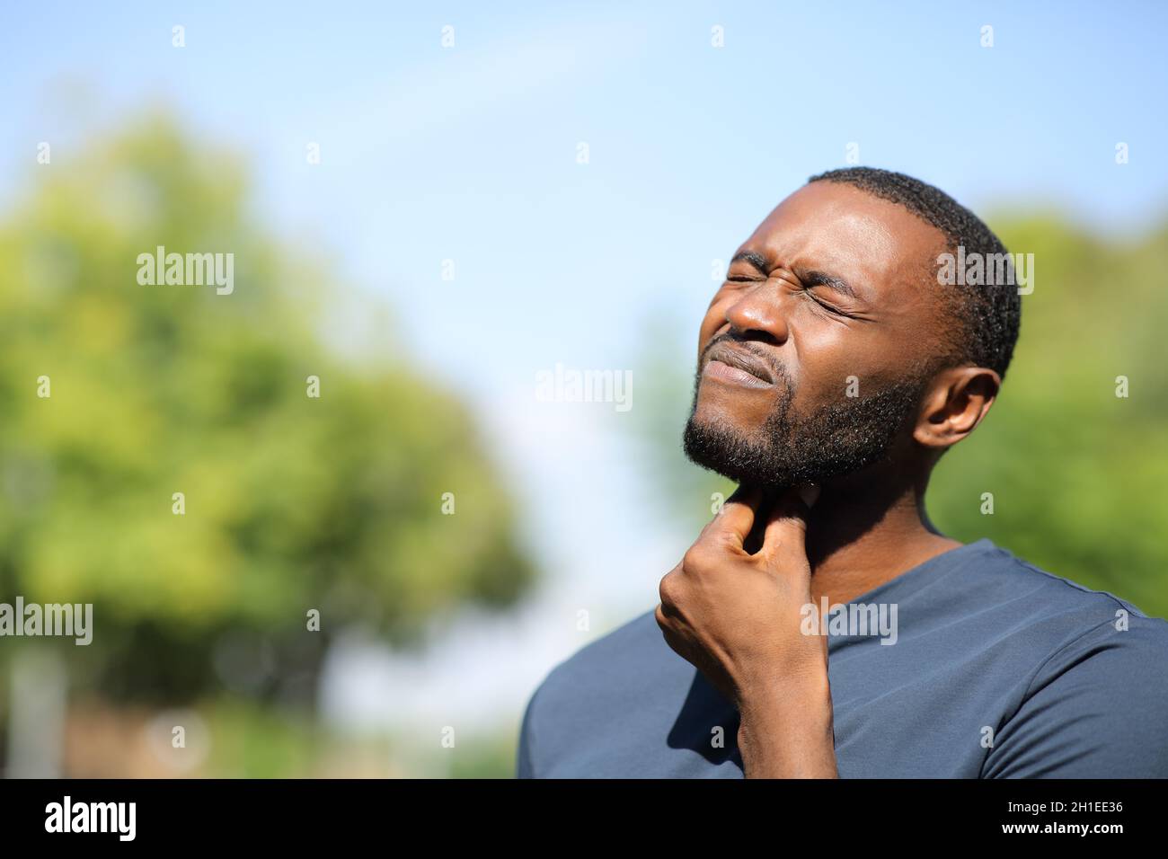 Homme à peau noire souffrant de mal de gorge debout dans un parc un jour ensoleillé Banque D'Images