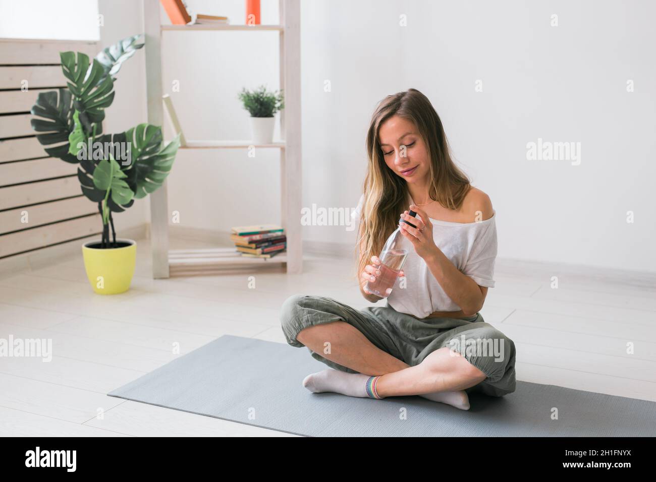 Jeune belle fille pratiquant le yoga au tapis, boire de l'eau pendant la pause. Concept de forme physique et de mode de vie sain. Banque D'Images