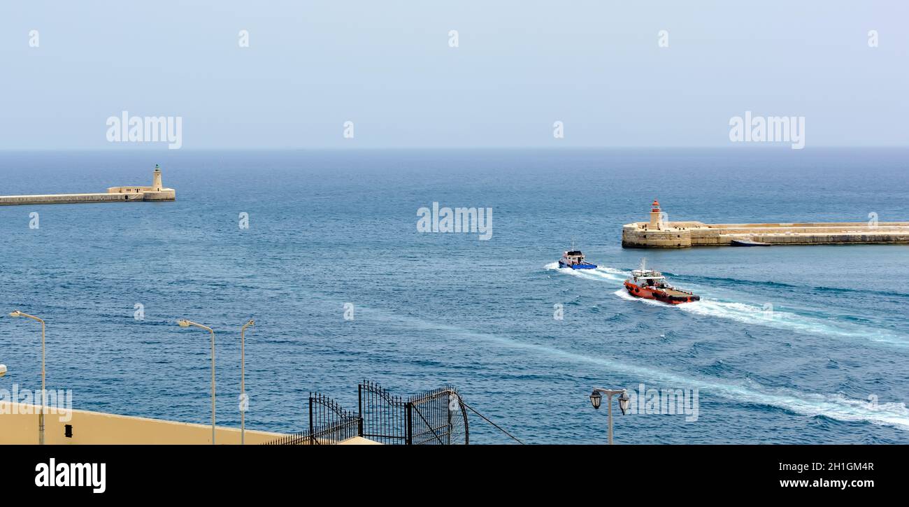 Bateaux allant dans l'eau de mer turquoise entre Valletta brise-lames avec phare et Ricasoli brise-lames lumière Banque D'Images