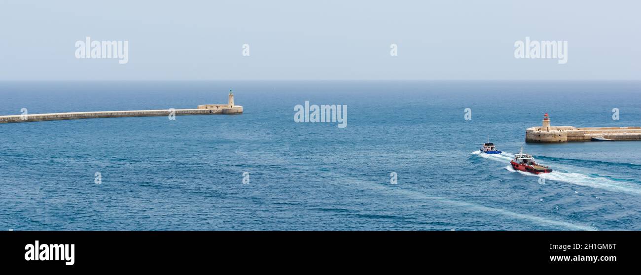 Bateaux allant dans l'eau de mer turquoise entre Valletta brise-lames avec phare et Ricasoli brise-lames lumière Banque D'Images