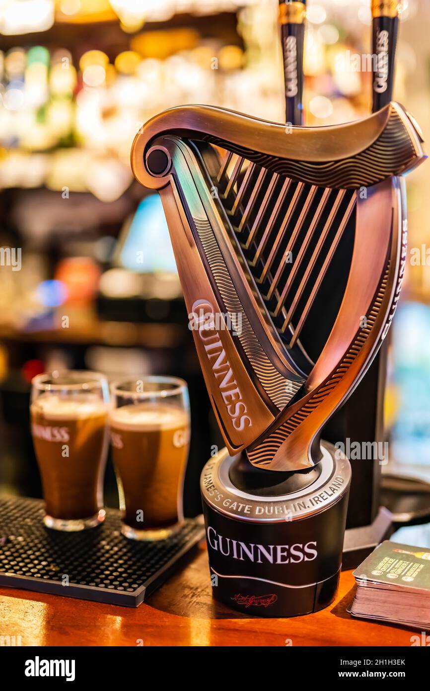 Dublin, Irlande, août 2018 mise au point sélective sur le robinet Guinness avec des pintes floues de bière mousseuse et un mur de bouteilles. La Guinness est une bière irlandaise emblématique Banque D'Images