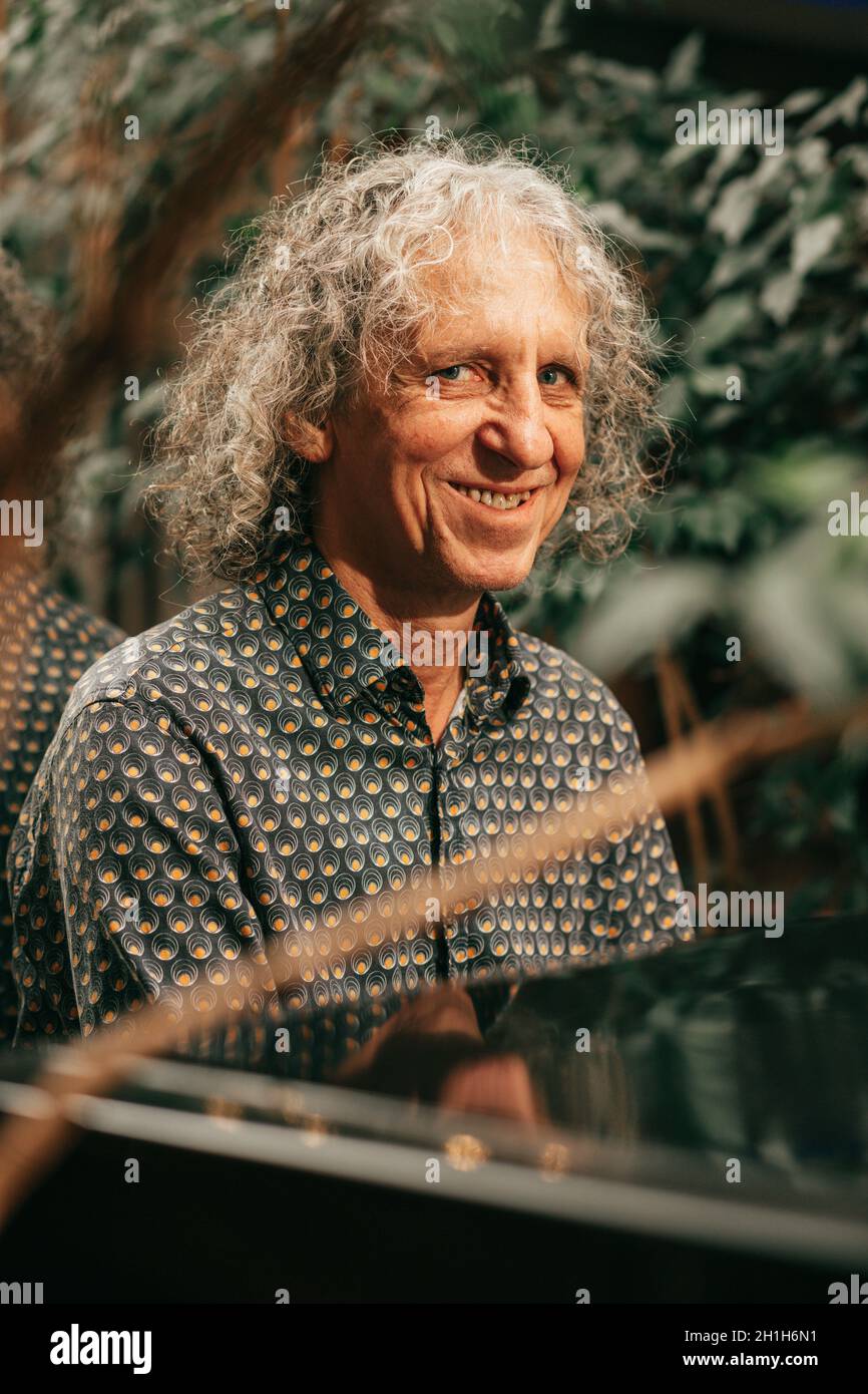 Portrait d'un homme mûr et souriant et attrayant, âgé de 65 ans, cheveux gris bouclés joue du piano et de la caméra looksat avec le sourire. Banque D'Images