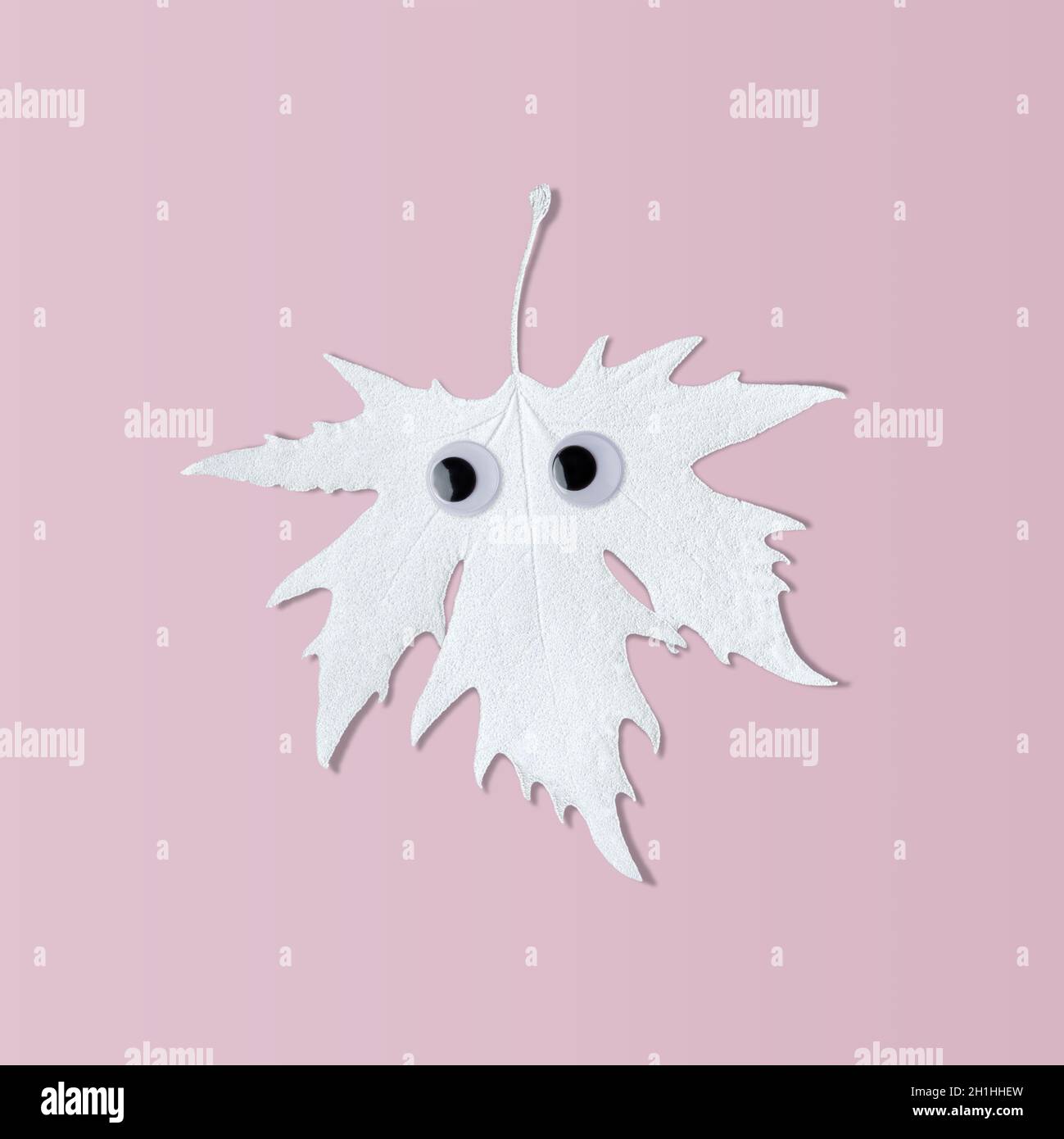 Feuille d'Halloween blanche avec des yeux drôles sur fond rose.Concept minimaliste amusant. Banque D'Images