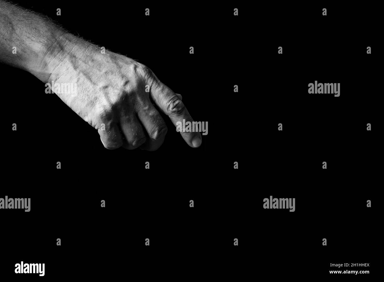 Image en noir et blanc d'un homme froissé pointant vers la main, paume vers l'extérieur, isolée sur un fond noir avec un éclairage spectaculaire. Banque D'Images