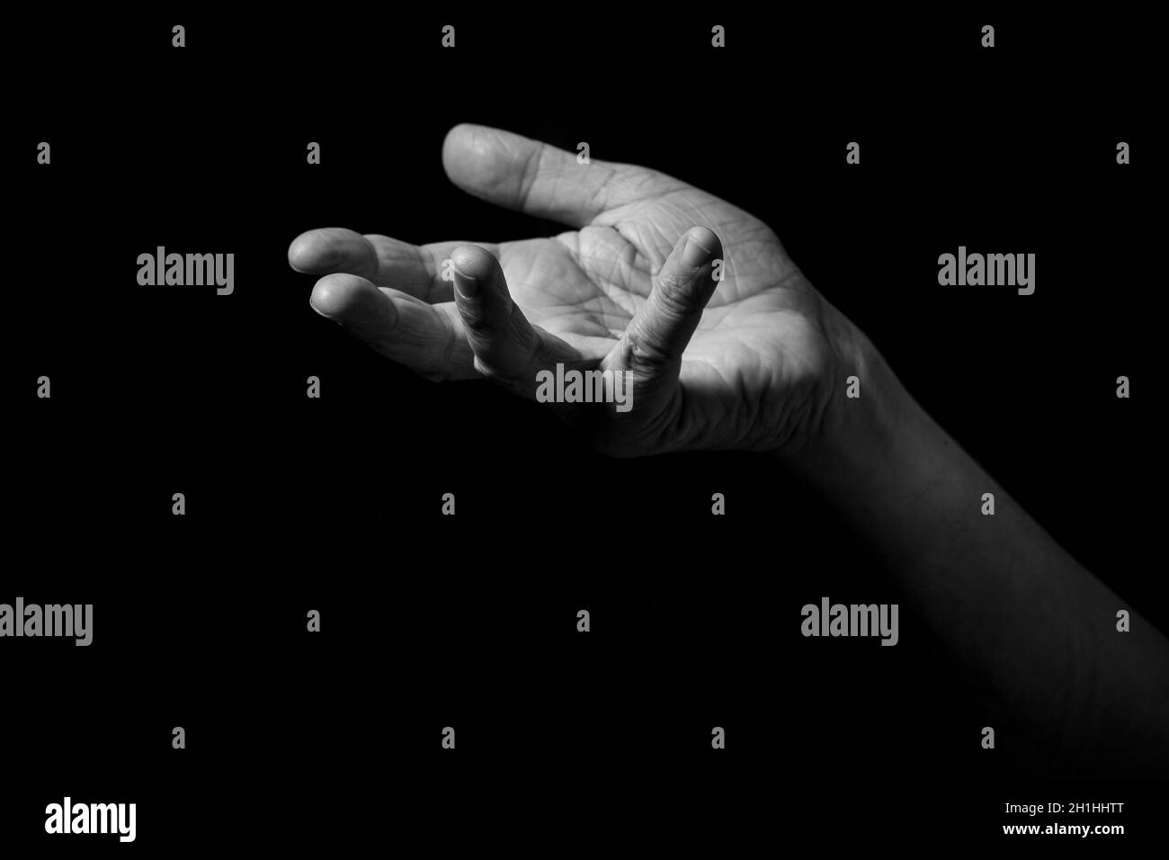 Image en noir et blanc de la main de l'homme ridée tenant des gestes avec paume ouverte, isolée sur un fond noir avec un éclairage spectaculaire. Banque D'Images