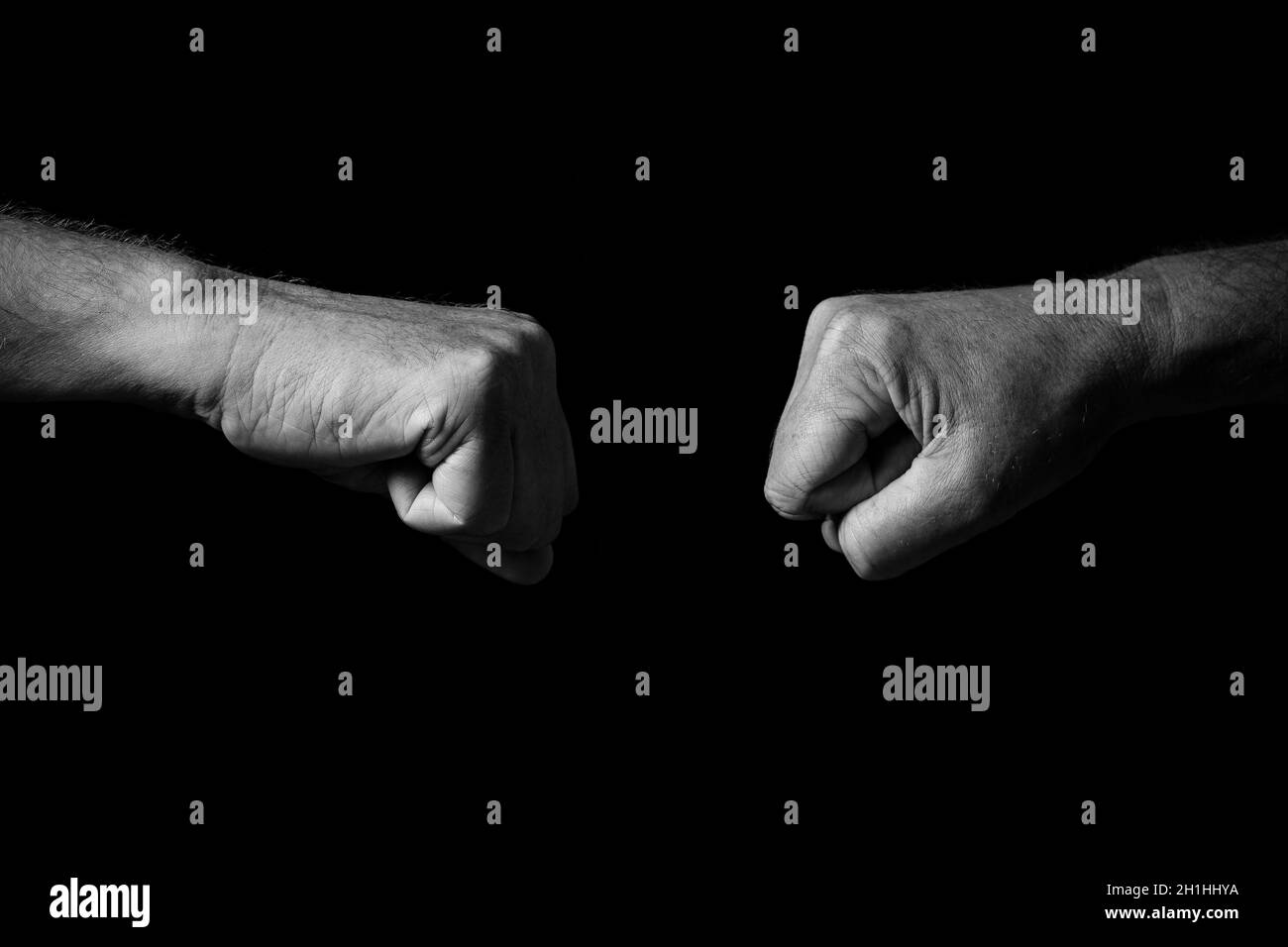 Image en noir et blanc des mains de sexe masculin froissées, maintenues par des poings serrés, pour des coups de poing ou de poing brumeux, isolées sur un fond noir avec une hauteur spectaculaire Banque D'Images