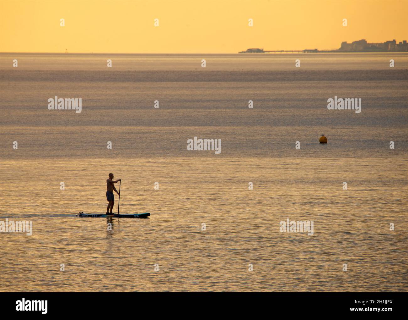 Paddleboarder silhouetted paddleboard d'une plage de Hove au coucher du soleil.Brighton & Hove, Englod, Royaume-Uni.Worthing Pier, West Sussex à l'horizon. Banque D'Images