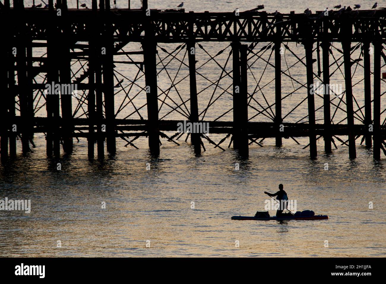 Pédalo en paddleboarder silhouetté autour de la jetée ouest abandonnée au coucher du soleil, Brighton, Angleterre.Construit en 1866 et fermé en 1975, le quai est toujours classé de catégorie I et un site bien connu. Banque D'Images