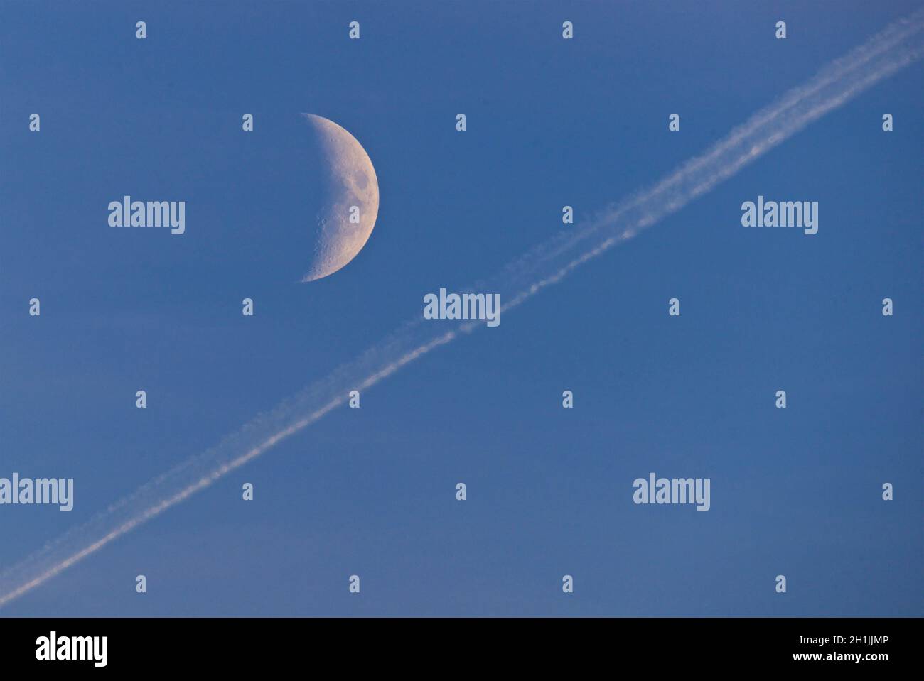 La lune (demi-croissant) et un air contrail dans un ciel bleu clair. Banque D'Images
