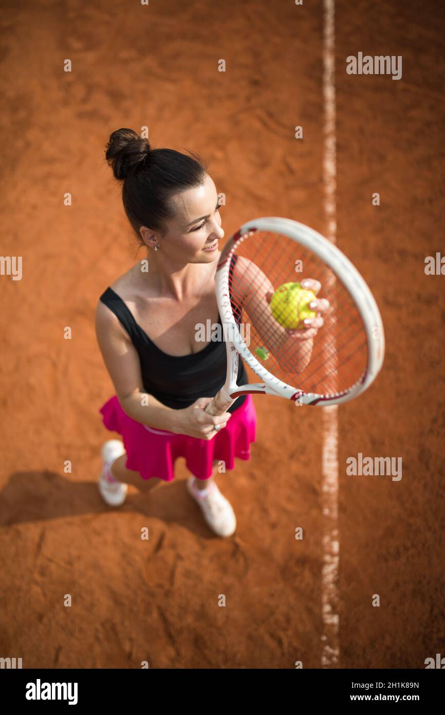 Vue de dessus d'un joli joueur de tennis pour jeune femme servant sur un court de tennis en argile. Intéressant POV shot - fille sportive pendant l'entraînement de tennis dans le clu Banque D'Images