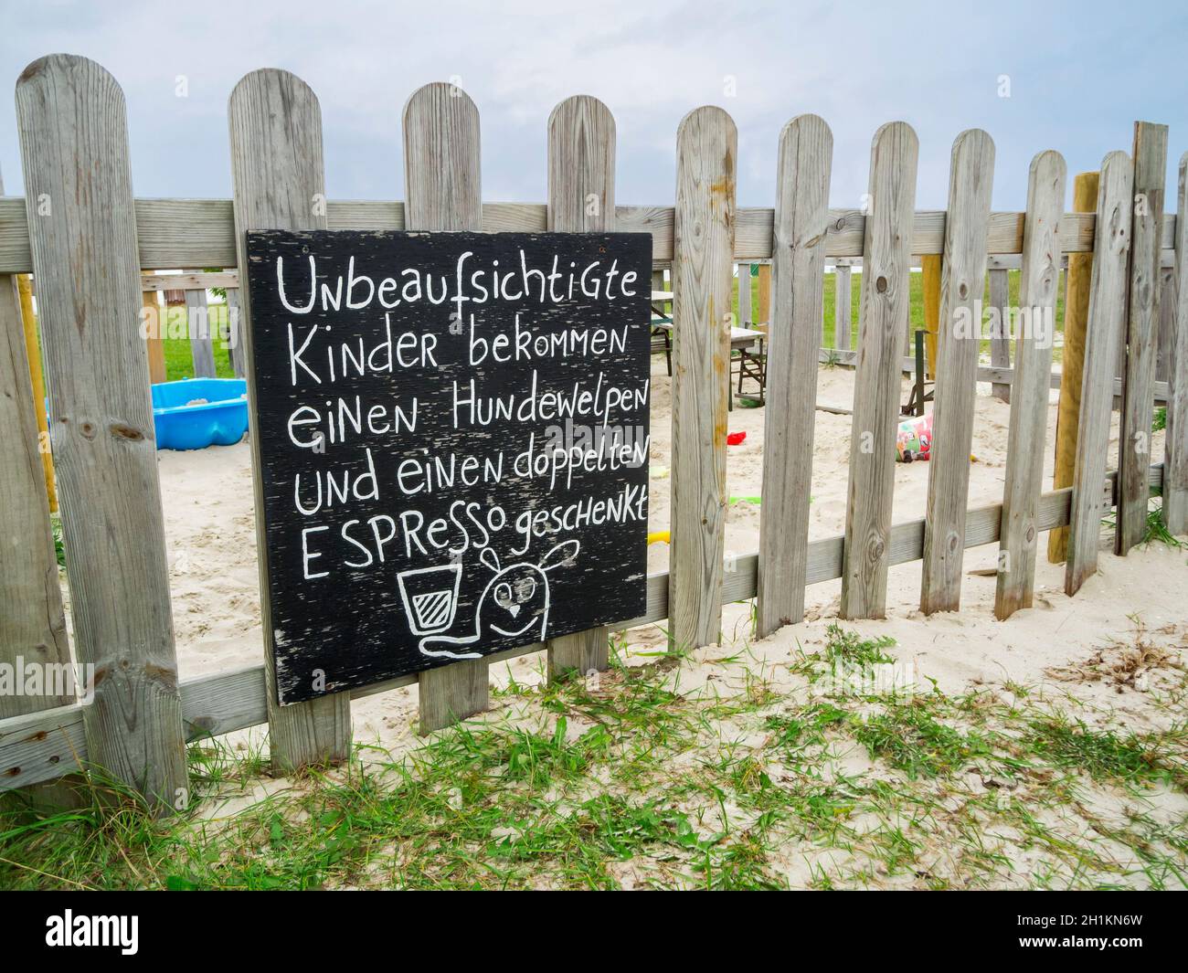 Weitwinkelansicht eines Sandkasten-Zauns mit der humorvollen Aufschrift (in deutschen Worten: 'Unbeaufsichtigte Kinder bekommen einen Hundewelpen un e Banque D'Images