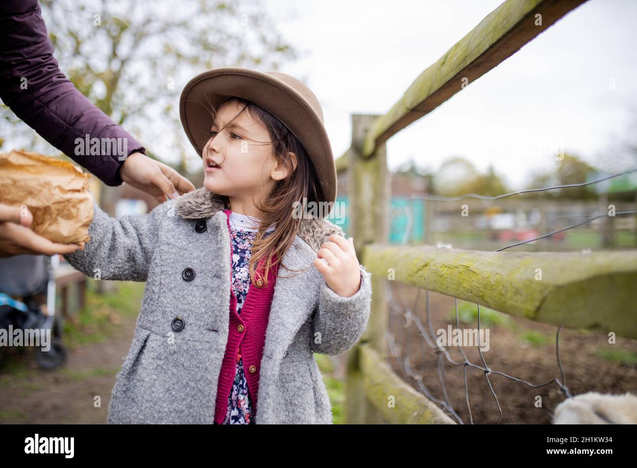 Bonne petite fille portant un chapeau de cowboy en interaction avec sa mère dans une ferme.Jeune fille aventureuse se préparant à nourrir les animaux de la ferme.Alimentation des animaux des baryards Banque D'Images