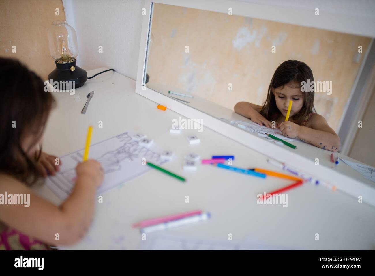 Une petite fille de brunette se réfléchit sur un miroir en face d'elle tandis qu'elle colore une image de la Statue de la liberté Banque D'Images