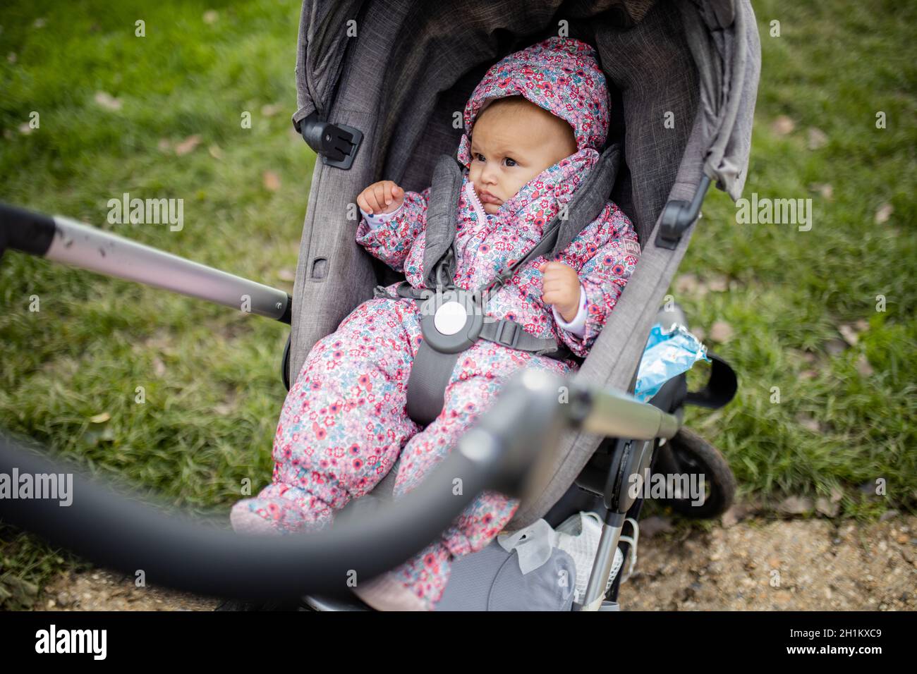 Bébé inquiet portant une combinaison à fleurs roses dans une poussette dans  un parc.Bébé inquiet assis dans une poussette dans le parc.Les tout-petits  qui se reposent Photo Stock - Alamy
