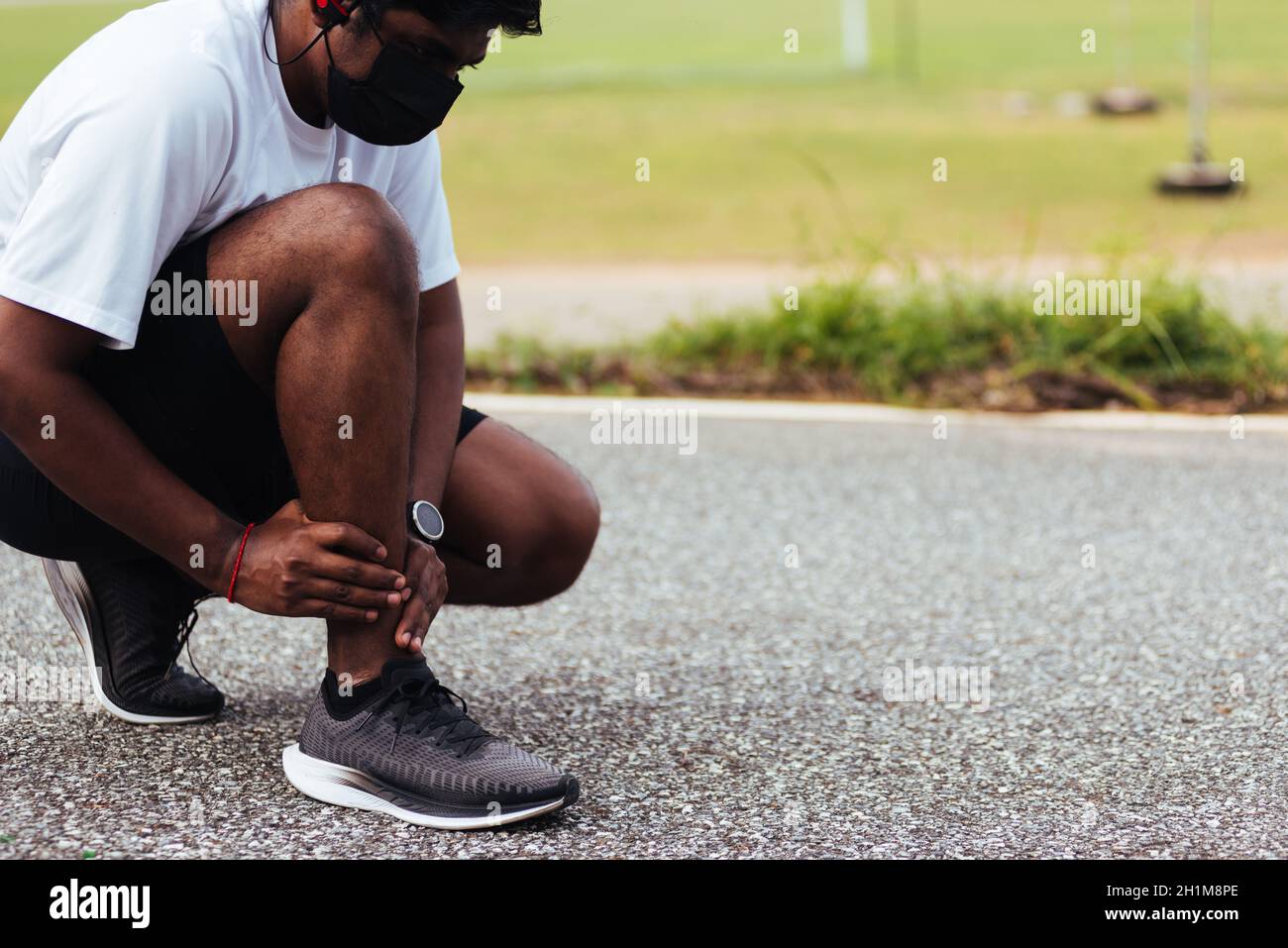 Gros plan asiatique jeune coureur sport noir homme porter montre mains joint tenir la douleur de jambe en raison de la cheville tordue cassé pendant la course à l'extérieur de la rue h Banque D'Images