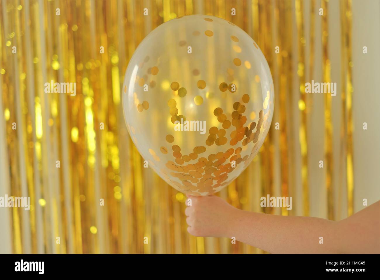 Vacances enfants.arrière-plan anniversaire.Ballon avec kanfeti d'or dans la main d'un enfant sur fond de tinsel d'or.Nouvel an et Noël. Festif Banque D'Images