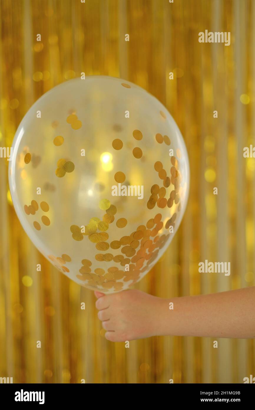 Vacances enfants.arrière-plan anniversaire.Ballon avec kanfeti d'or dans la main d'un enfant sur fond de tinsel d'or.Nouvel an et Noël. Festif Banque D'Images