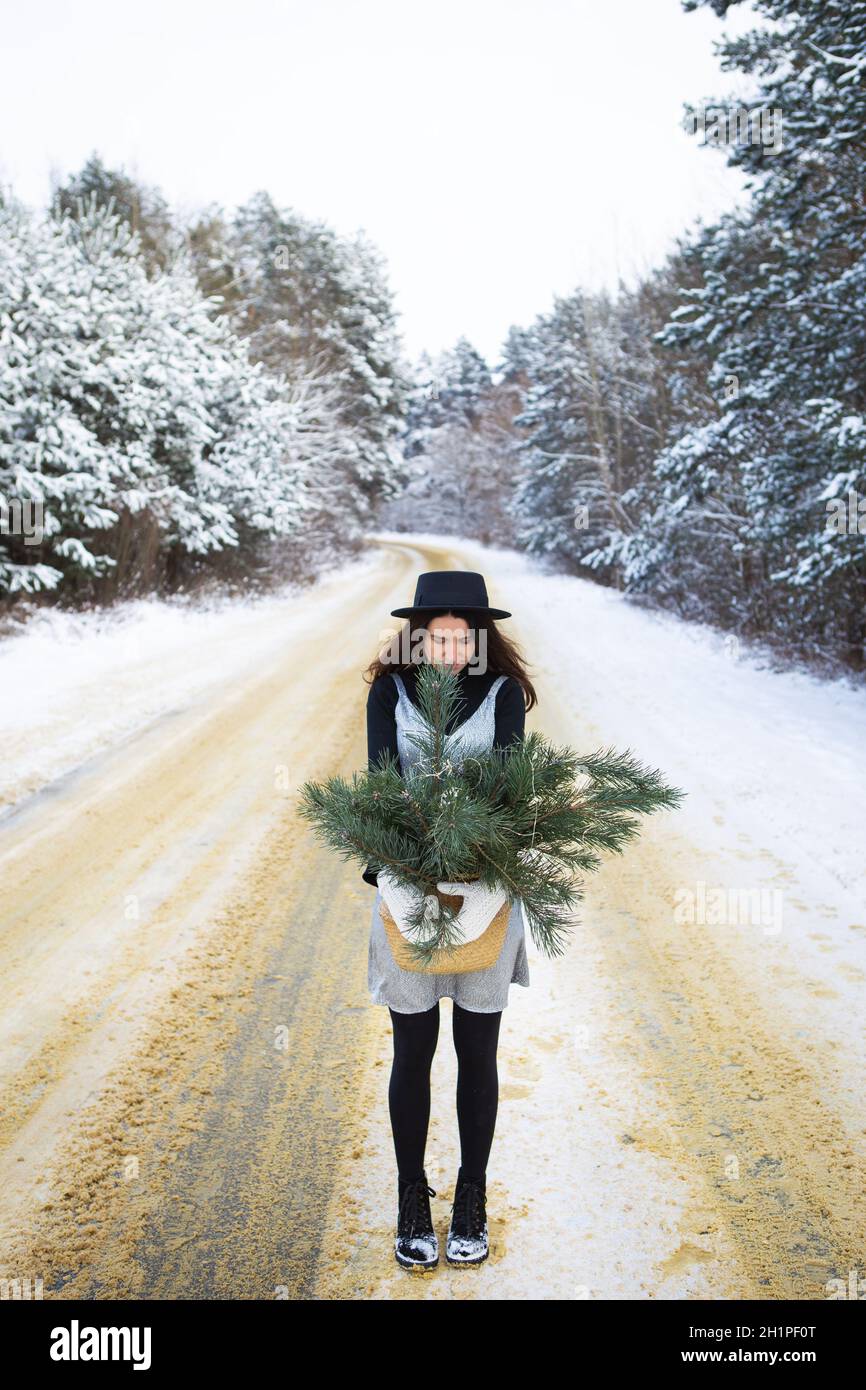 Une jeune fille dans une robe argentée et des supports de chapeau avec son dos au milieu d'un bel hiver route dans la forêt Banque D'Images
