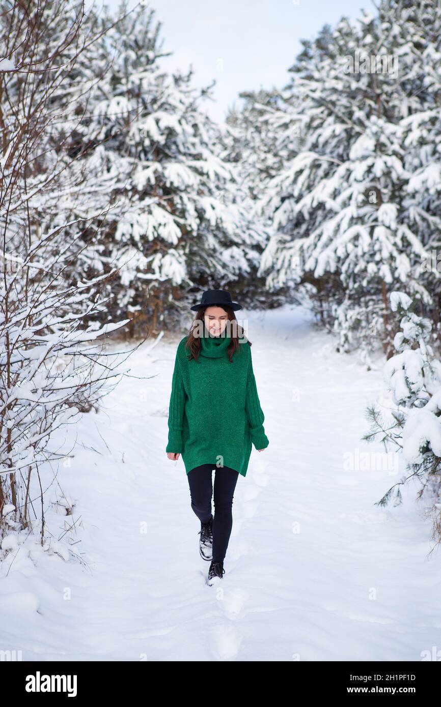 Une jeune fille dans un chandail vert foncé et un chapeau se dresse au milieu d'une belle forêt d'hiver Banque D'Images