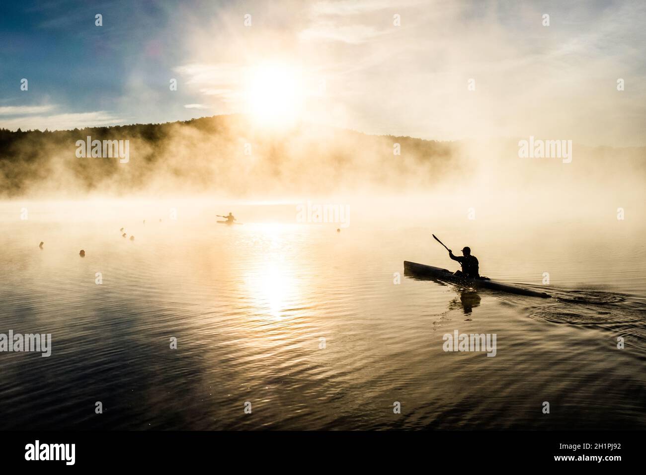 Kayakistes silhouettés par le soleil levant sur le lac Iroquois dans le Vermont, États-Unis, Nouvelle-Angleterre, un matin brumeux de septembre. Banque D'Images