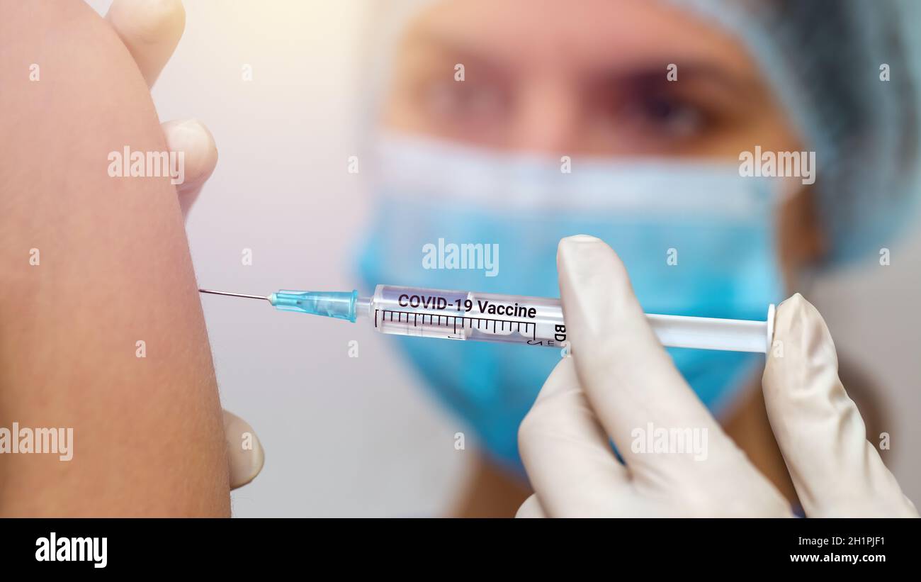 Infirmière féminine en masque chirurgical bleu injectant le vaccin contre le covid-19 dans l'épaule du patient de près. Concept de lutte contre la pandémie du coronavirus. Banque D'Images