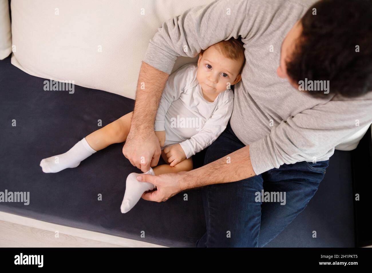 Le jeune père met des chaussettes sur son fils, assis sur un canapé. Banque D'Images