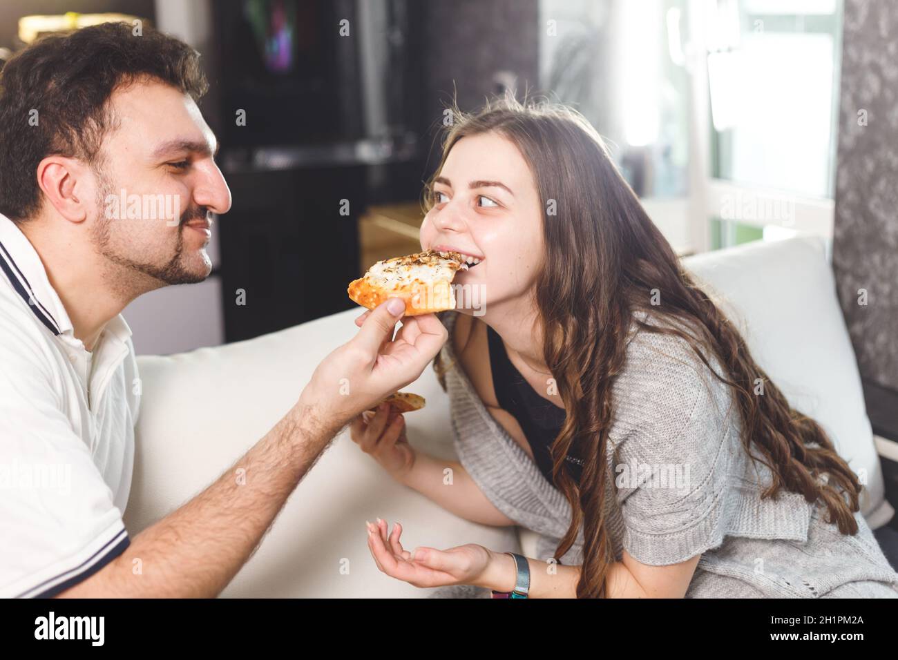 Couple heureux à la maison se nourrissant les uns les autres avec de la pizza Banque D'Images