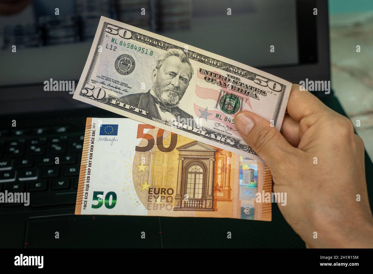 Une main contenant deux billets, l'un de cinquante dollars américains et l'autre de cinquante euros Banque D'Images