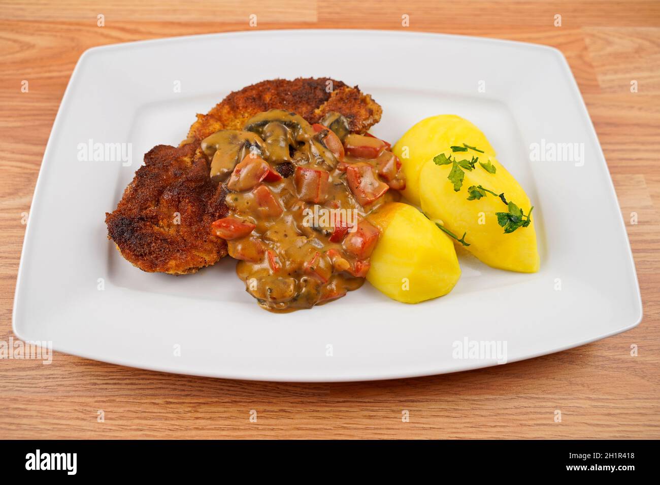 porc pané aux pommes de terre et aux champignons, sauce paprika sur une assiette de service blanche Banque D'Images