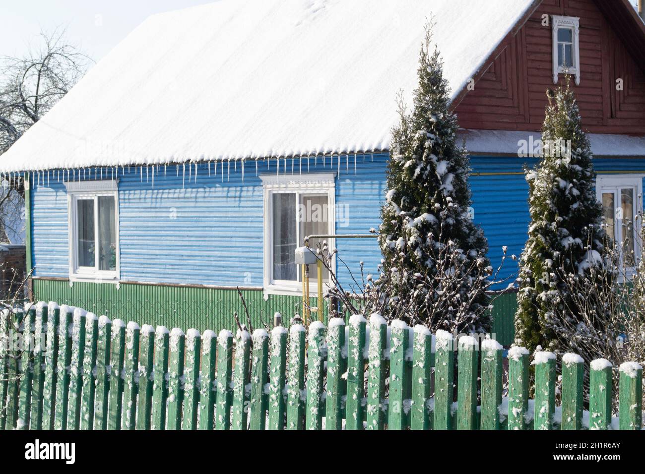 Ancienne maison en bois dans le village biélorusse.Maison en bois avec une clôture faite de planches avec de l'épinette verte en hiver. Banque D'Images