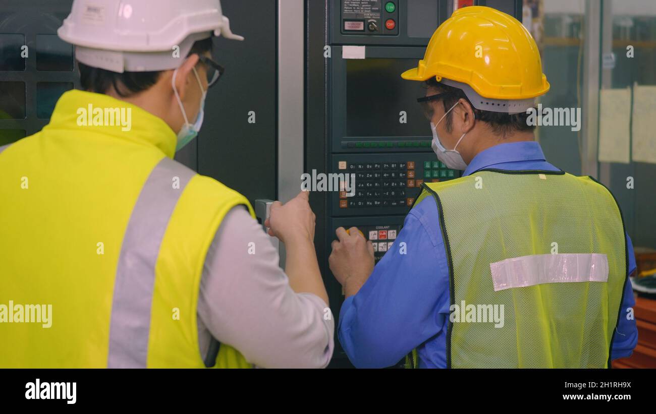 Ouvrier d'usine asiatique travaillant la programmation automatique CNC de commande de fraisage centre de l'industrie des machines dans l'atelier de fabrication d'outils avec un ingénieur Banque D'Images