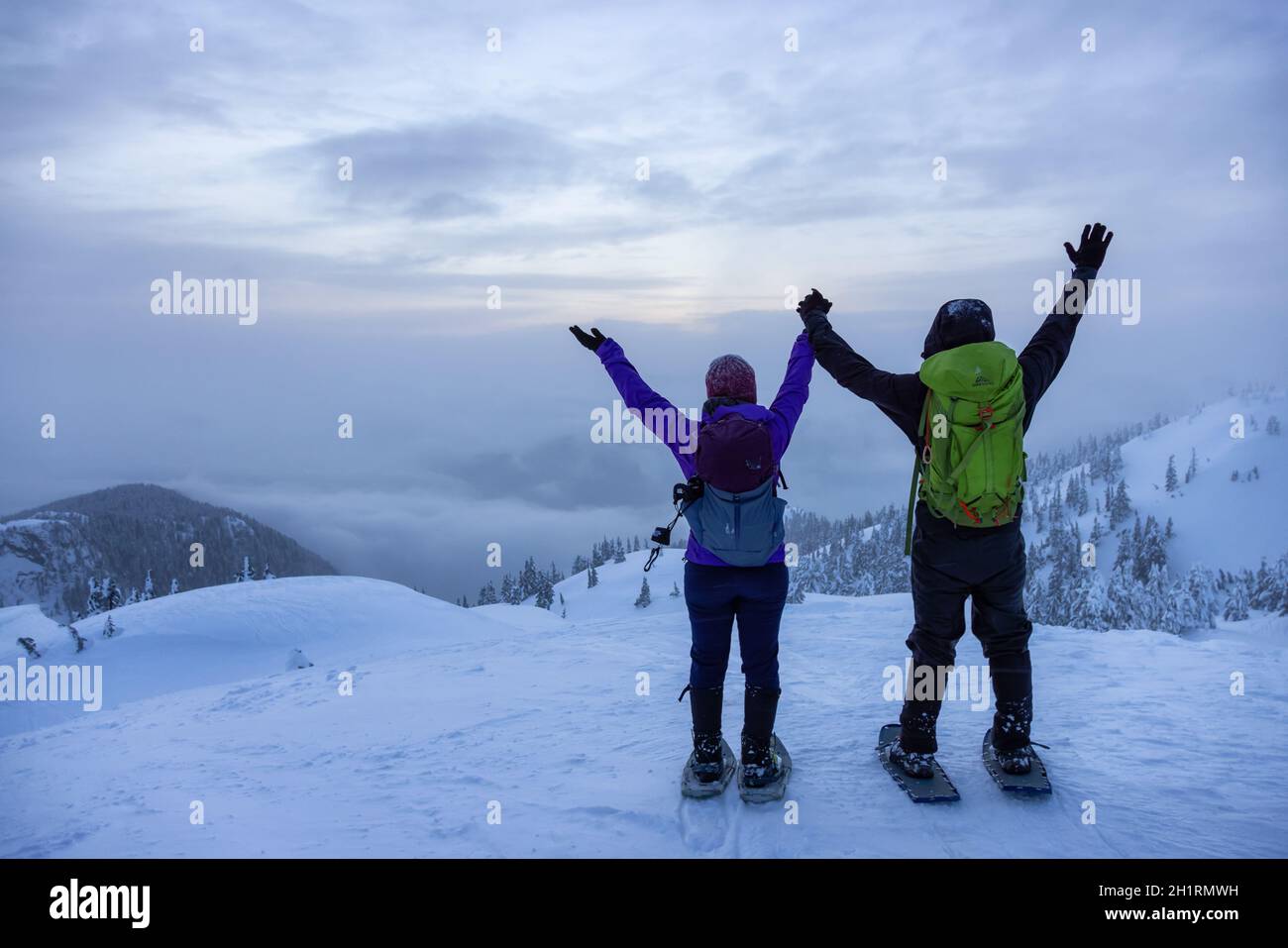 North Vancouver, Colombie-Britannique, Canada - 13 février 2021 : couple aventureux au sommet de Seymour Mountain pendant le coucher du soleil hivernal enneigé. Banque D'Images