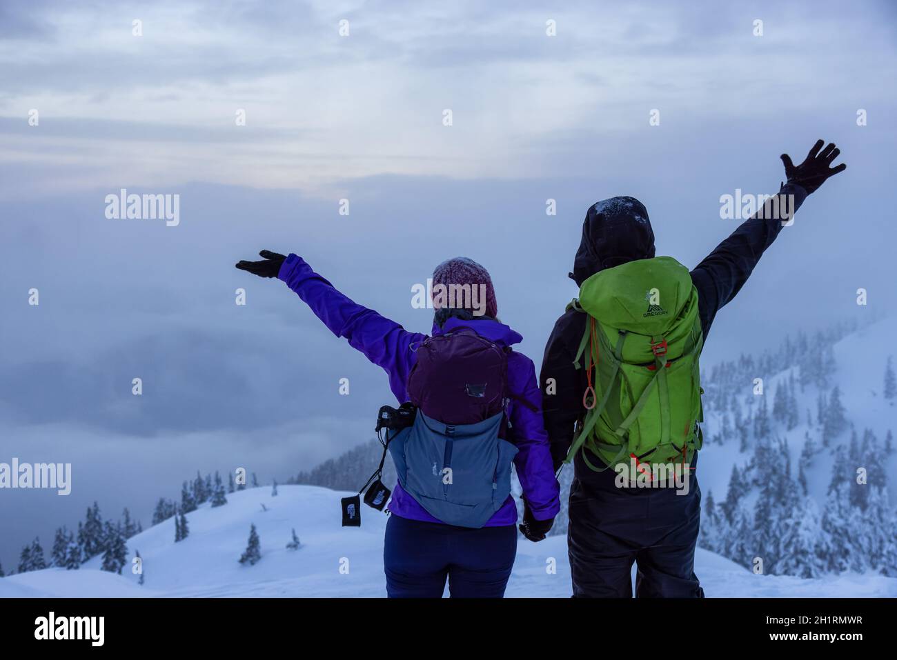 North Vancouver, Colombie-Britannique, Canada - 13 février 2021 : couple aventureux au sommet de Seymour Mountain pendant le coucher du soleil hivernal enneigé. Banque D'Images
