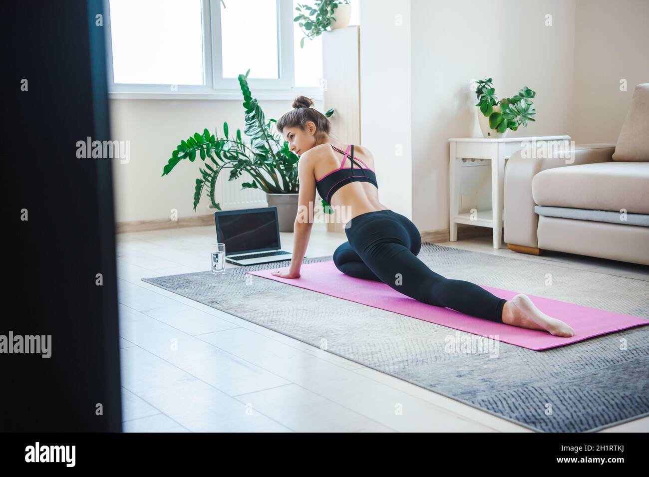 Placez la femme dans des vêtements de sport qui s'étirent les jambes, s'entraîner avec un ordinateur portable, regarder des tutoriels en ligne, pratiquer des pilates sur un tapis de yoga.Restez en forme Banque D'Images