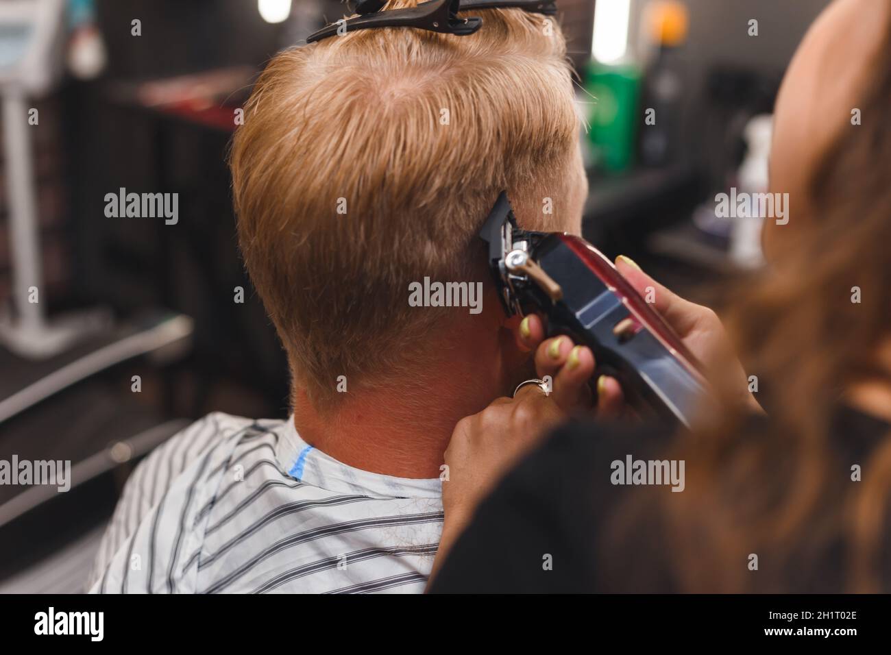 Le masque de coiffeur féminin coupe les poils d'un homme avec une tondeuse à cheveux. Coiffure pendant la prise de distance sociale. Banque D'Images