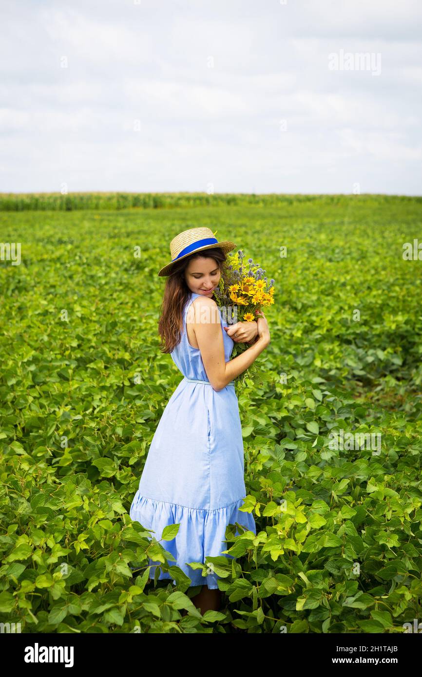 la fille est debout dans le champ avec un bouquet de fleurs jaunes et un chapeau de paille. Banque D'Images