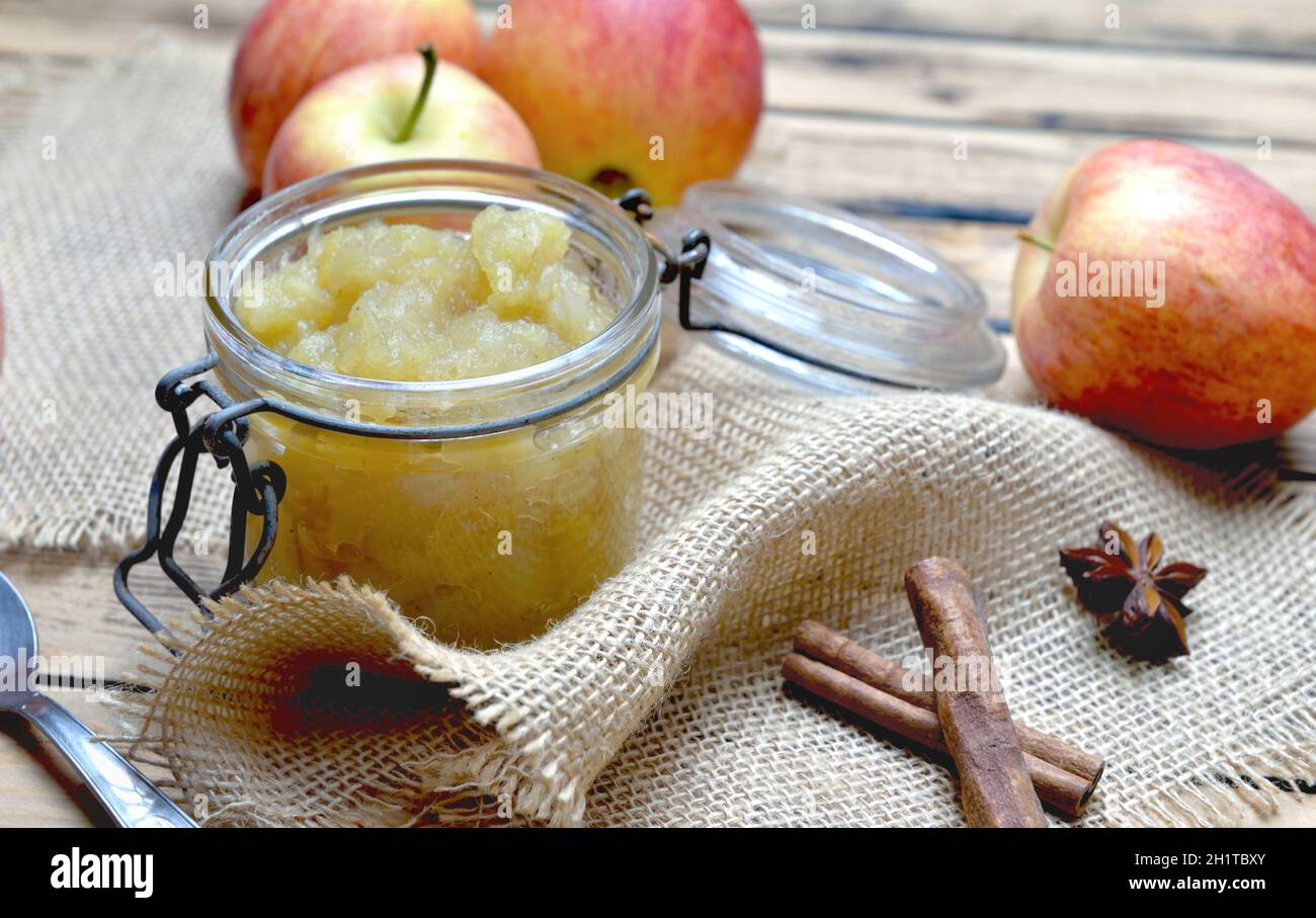 sauce aux pommes maison dans un pot en verre avec des pommes rouges et un bâton de cannelle sur une table en bois Banque D'Images